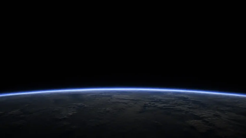 Earth’s curved horizon seen from orbit with a thin blue atmospheric layer above the dark surface.