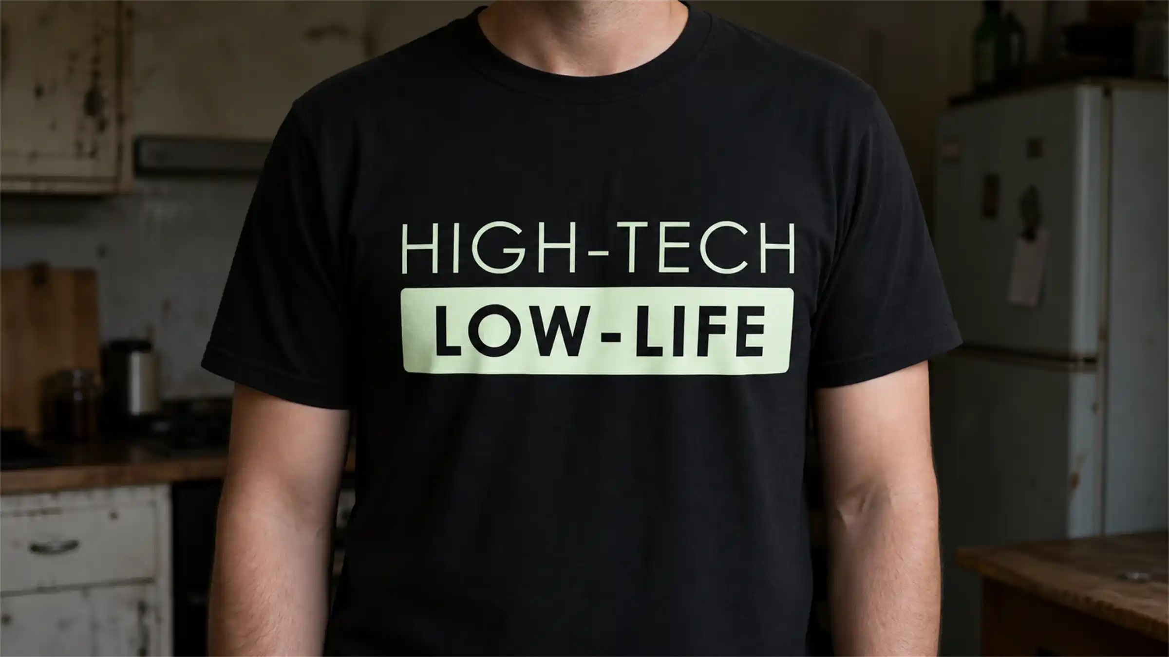 A man in a black t-shirt printed HIGH-TECH over LOW-LIFE in pale green, standing in a worn, dimly lit kitchen.